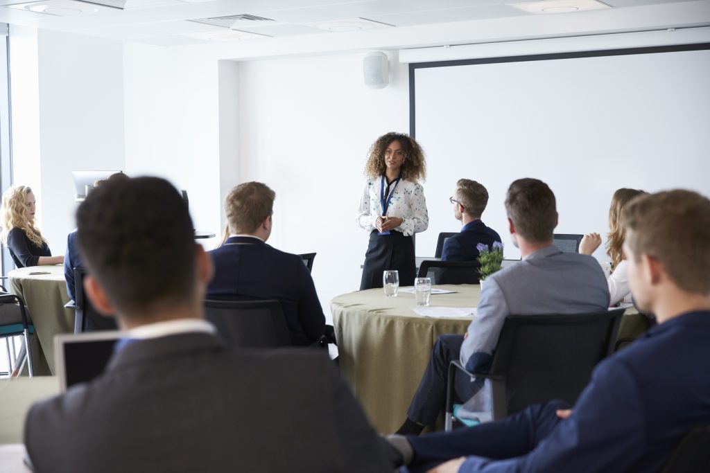 A professional young woman speaking in front of an audience about the benefits of marketing