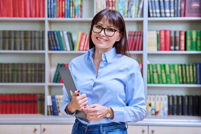 A young woman with glasses holding a laptop thinking about digital marketing for authors